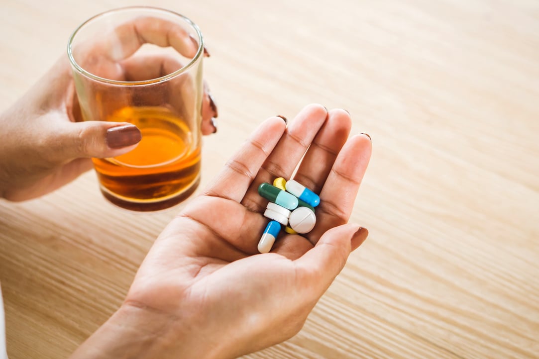 Unhealthy Lifestyle: Woman's Hand Taking Pills with a Glass of Alcohol in Close-up